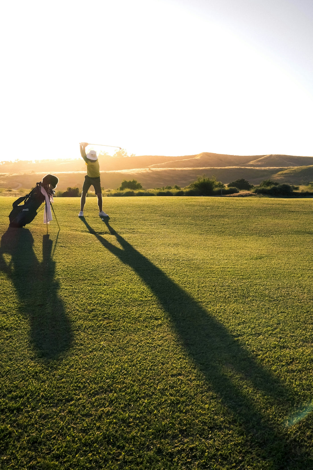 A golfer swinging a club on a green course at low sun