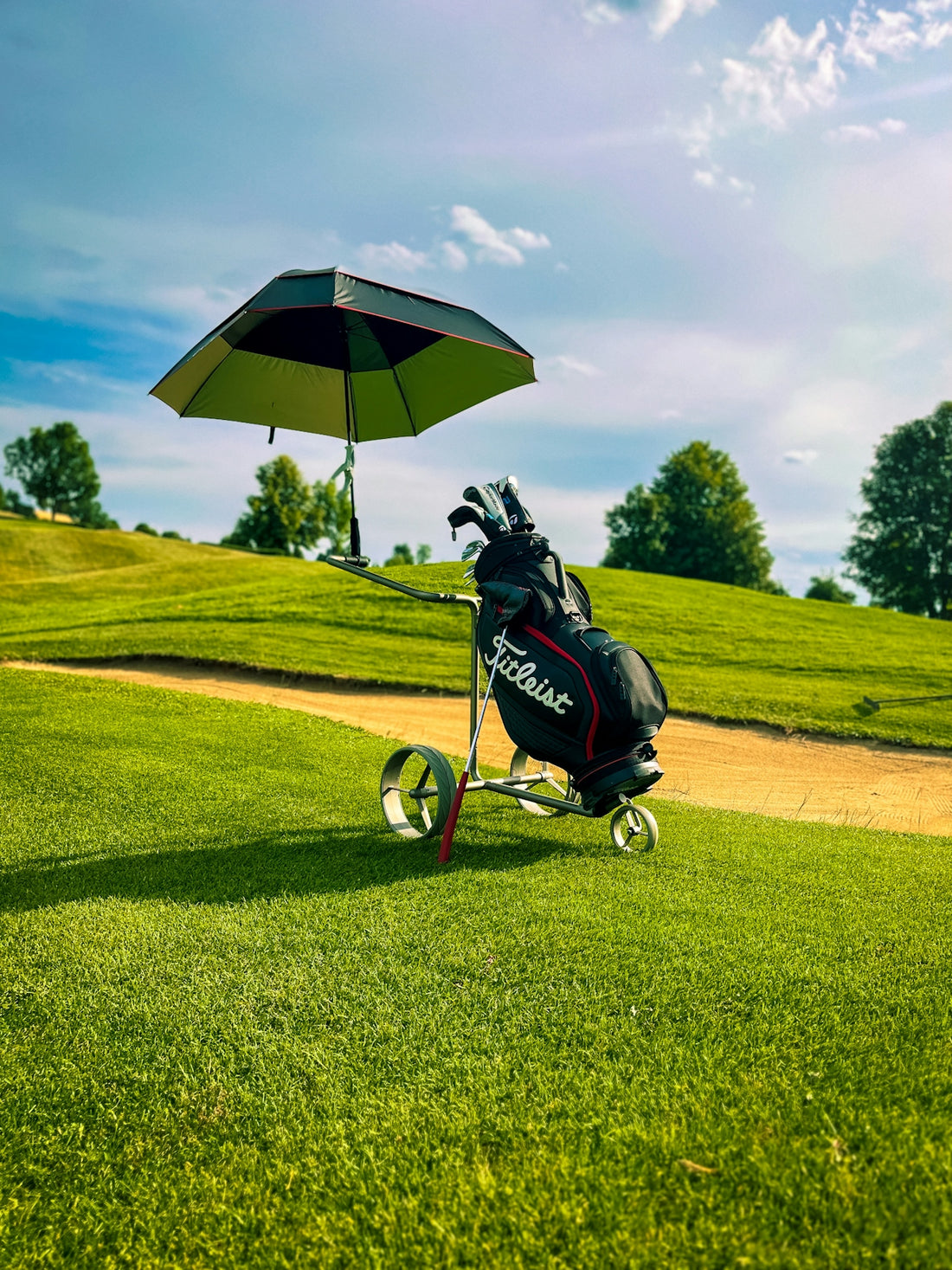 Golf bag with umbrella sits on a sunny golf course.