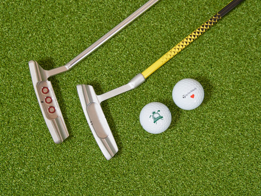 Two golf putters and two golf balls on grass.