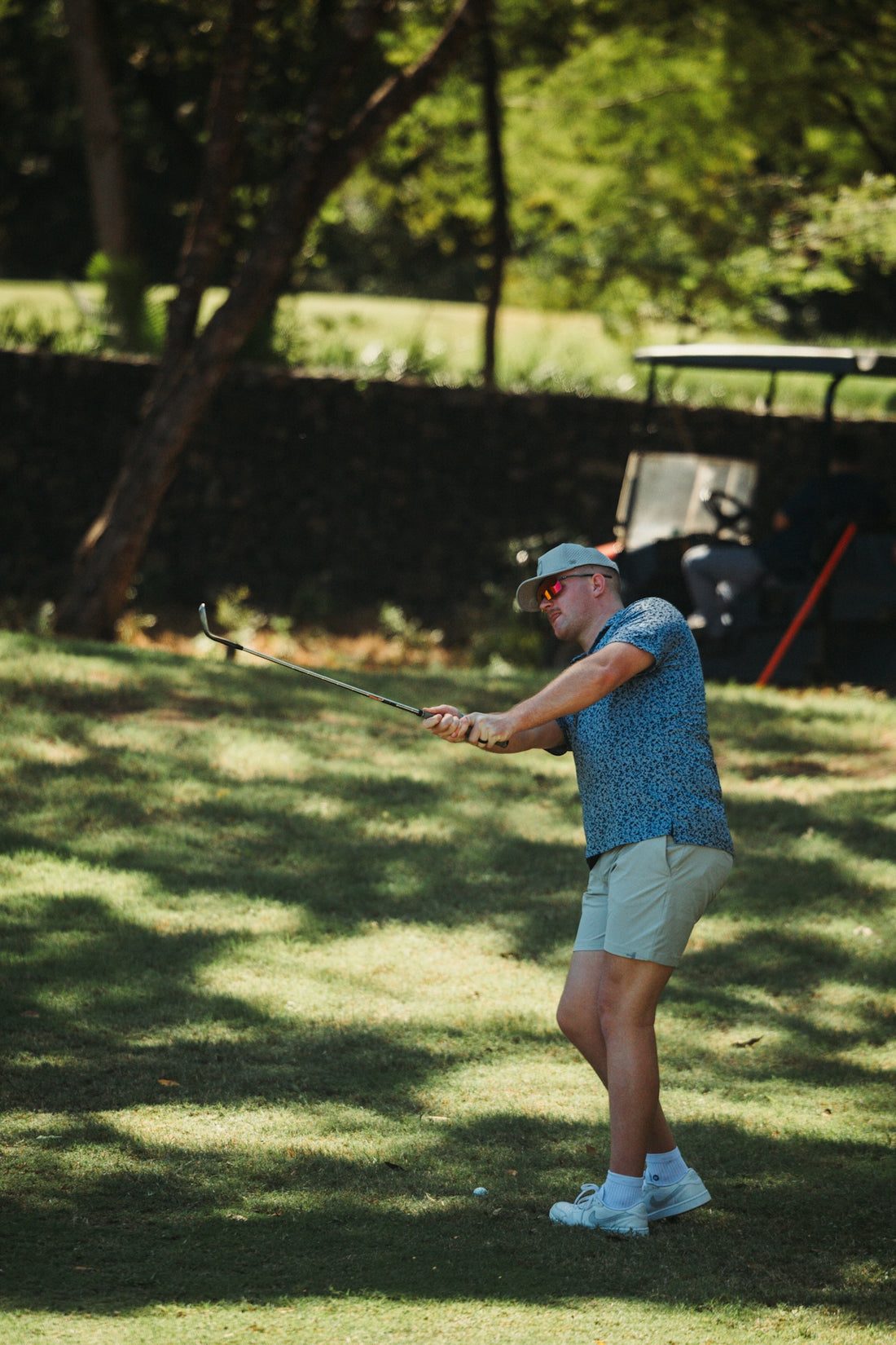 Man swinging golf club on grassy field with golf cart.