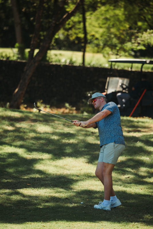 Man swinging golf club on grassy field with golf cart.