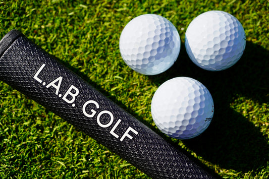 Golf club grip and three white golf balls on grass
